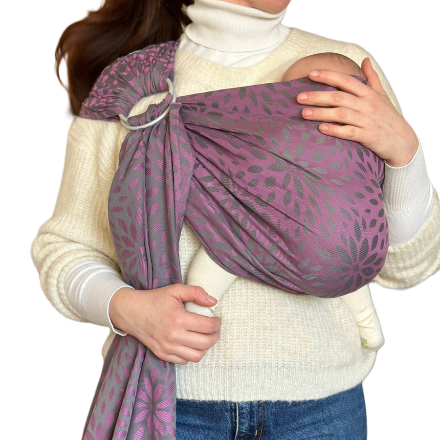 Ringsling KAAMI Sling Flora Purple Grape: Eine Frau trägt ihr Baby vor der Brust, an der Schulter läuft das Tuch durch zwei Ringe.