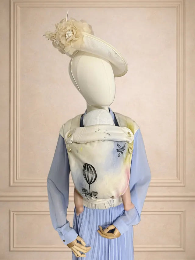 Handbemalte MonDoudou „Toile d’Amour“ an einer Büste mit Hut, vor einer getäfelten Wand.