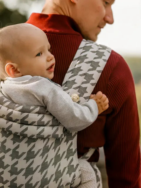 Un père porte son enfant sur le dos dans le MonDoudou Très Chic, l’enfant regarde par-dessus son épaule.
