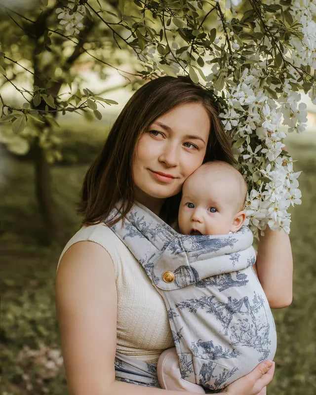 La porteuse tient son enfant dans le MonDoudou Toile de Jouy, joue contre joue, au-dessus d’eux des fleurs blanches.